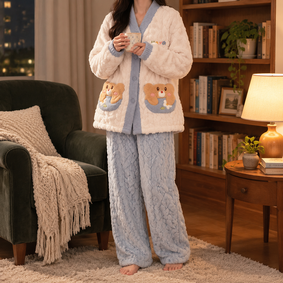 Frau im Flanell Pyjama Damen mit Knopfjacke in Creme und Blau und blauer Hose steht mit Tee in der Leseecke am Abend