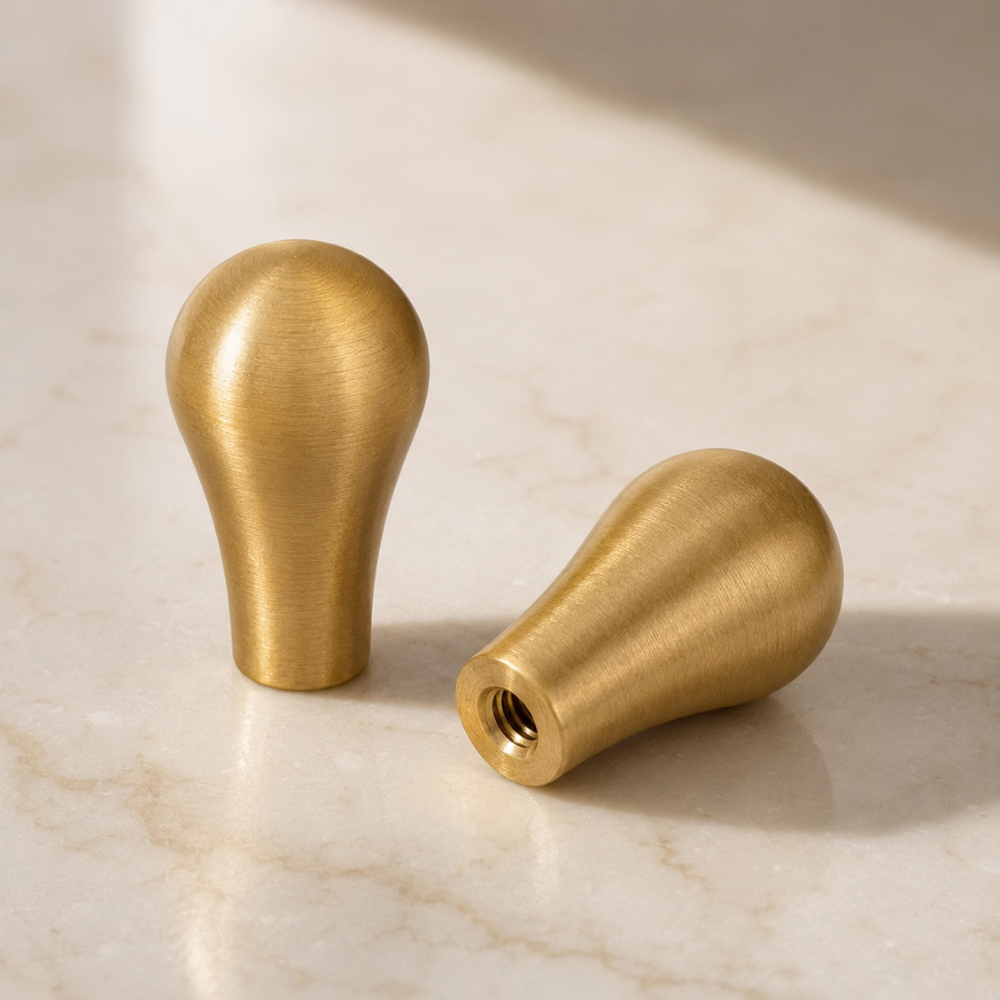 Zwei goldene Möbelknöpfe in Tropfenform auf Marmor