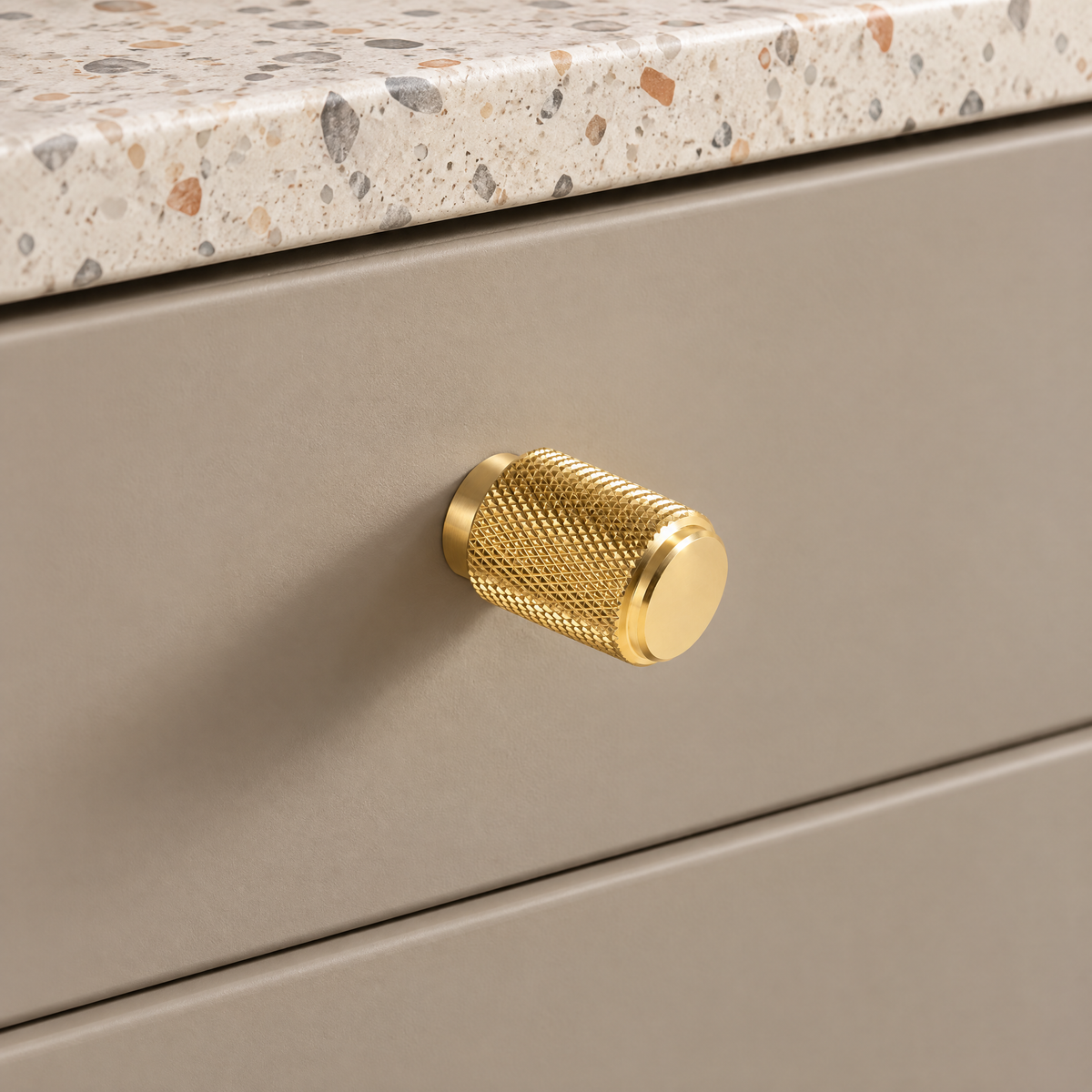 Möbelknöpfe rund in Gold: gerändelter Zylinderknopf an einer taupefarbenen Badschublade mit Terrazzo-Platte