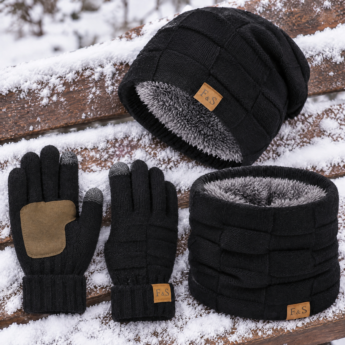 Schwarzes Mütze Schal Set auf einer verschneiten Bank: Handschuhe mit PU Besatz an der Handfläche, Beanie und Schlauchschal mit grauem Fleecefutter