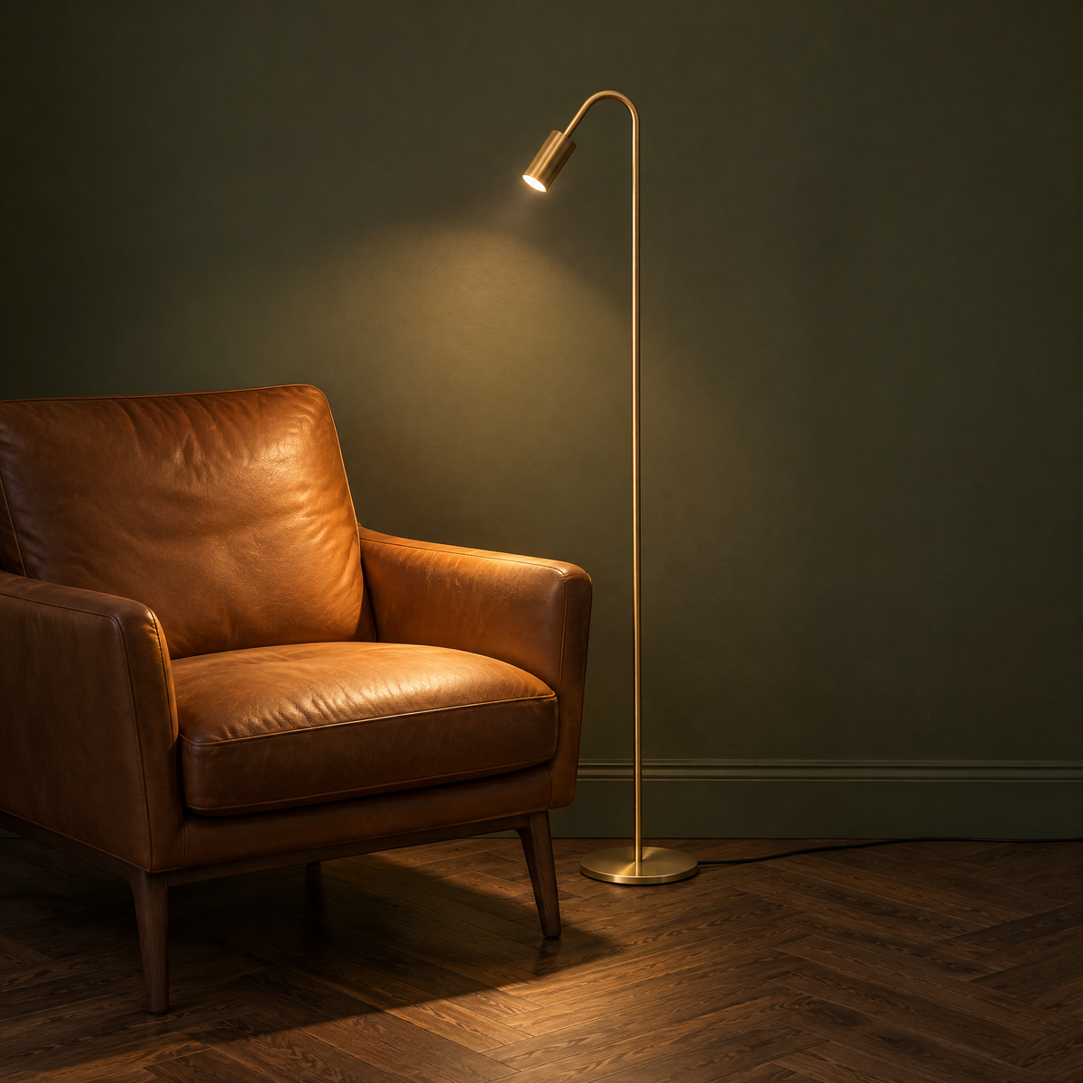 Geschwungene Stehlampe aus Kupfer in Gold als Leselampe neben einem Ledersessel, eingeschaltet mit warmem Lichtkegel