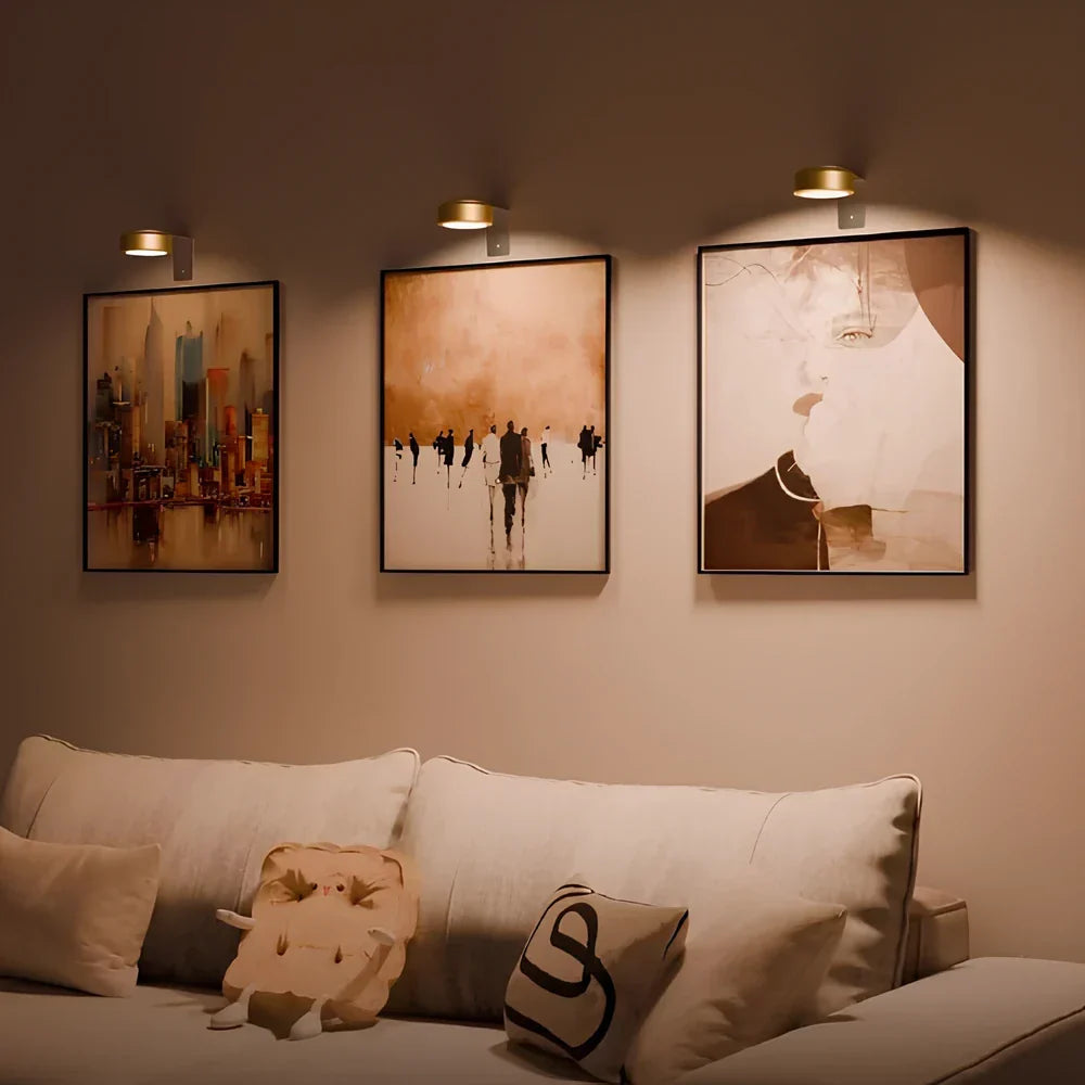 Goldene Wandleuchten über drei gerahmten Bildern im Wohnzimmer