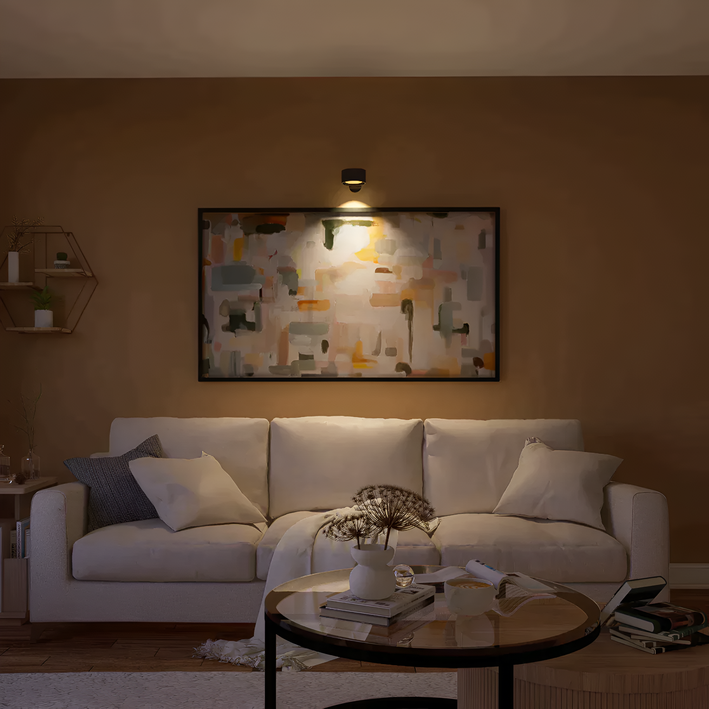 A cozy living room with a white sofa, abstract painting above, and a lit sconce. A coffee table with a plant and magazine sits in front. Shelves with plants are on the left wall.