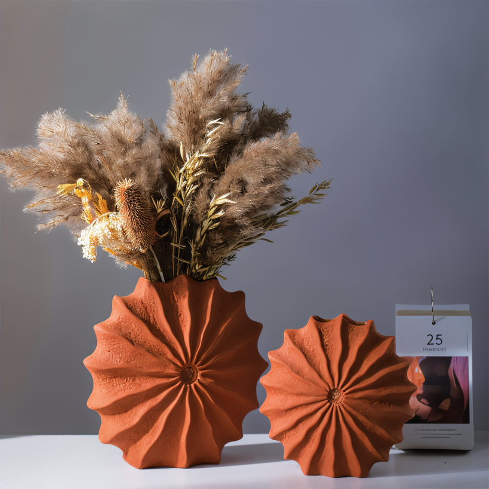 Textured terracotta vases with a radial design holding dried pampas grass, styled on a white surface with a modern desk calendar