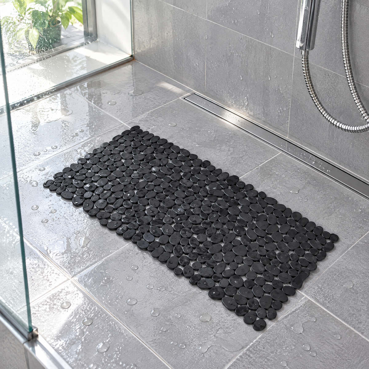 Schwarze Duschmatte in Kieselstein-Optik auf grauen Fliesen in einer begehbaren Dusche mit Wassertropfen