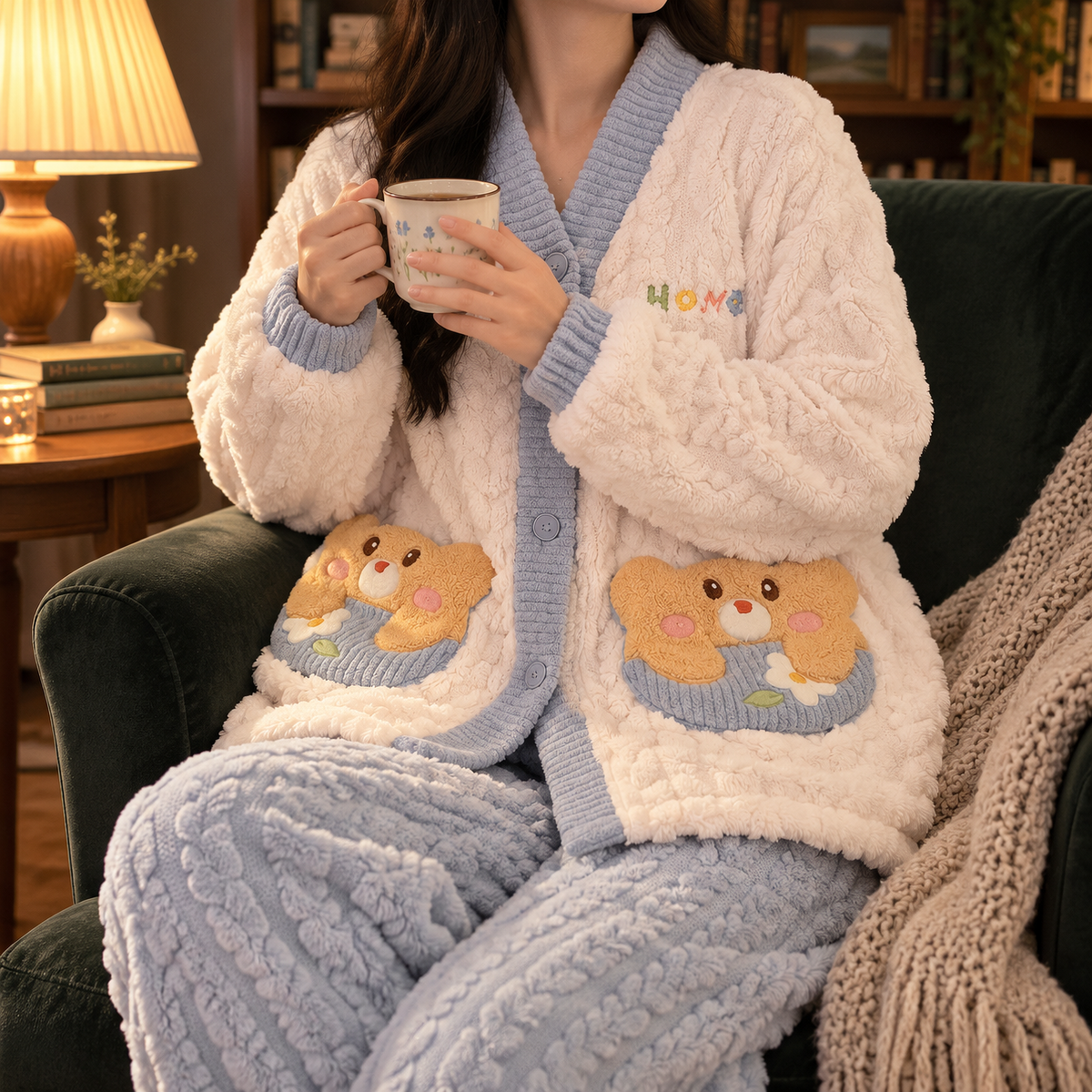 Frau im Flanell Pyjama Damen in Creme und Blau mit Teddy-Applikationen an den Taschen sitzt mit Teetasse im Sessel neben einer Tischlampe