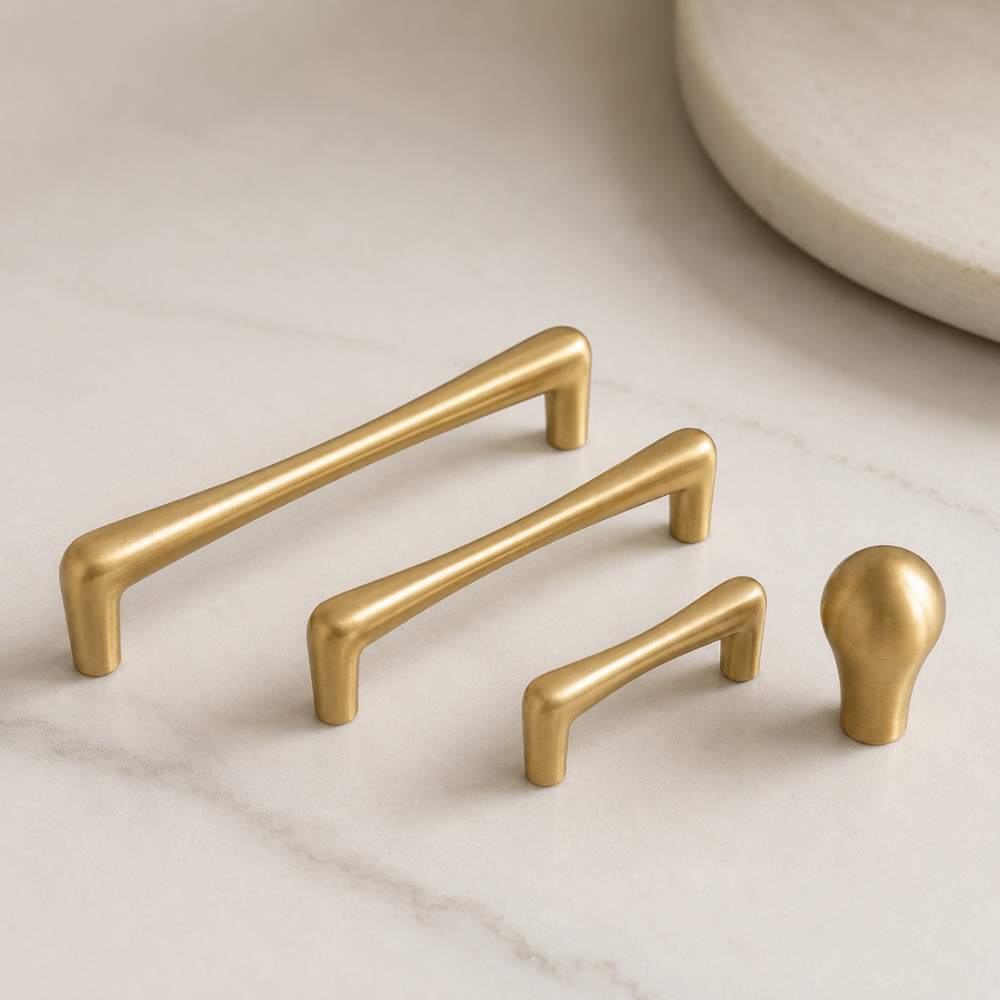 Goldene Griffe in drei Größen und Knopf in Tropfenform auf hellem Marmor