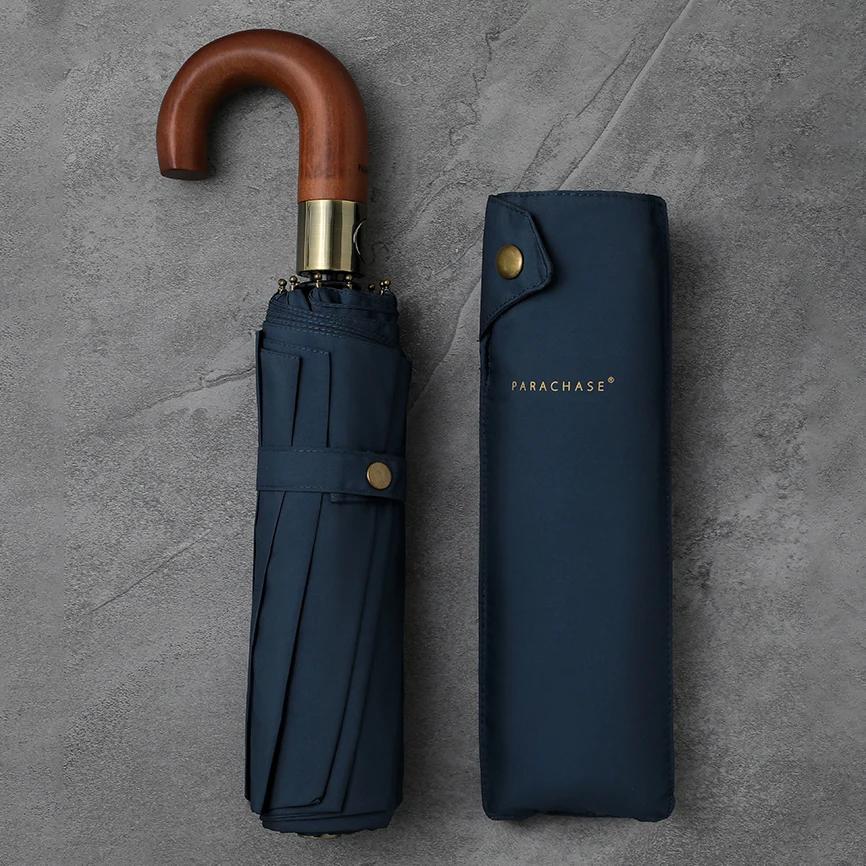 Regenschirm in Navy, zusammengeklappt mit Holzgriff, neben der passenden Schutzhülle