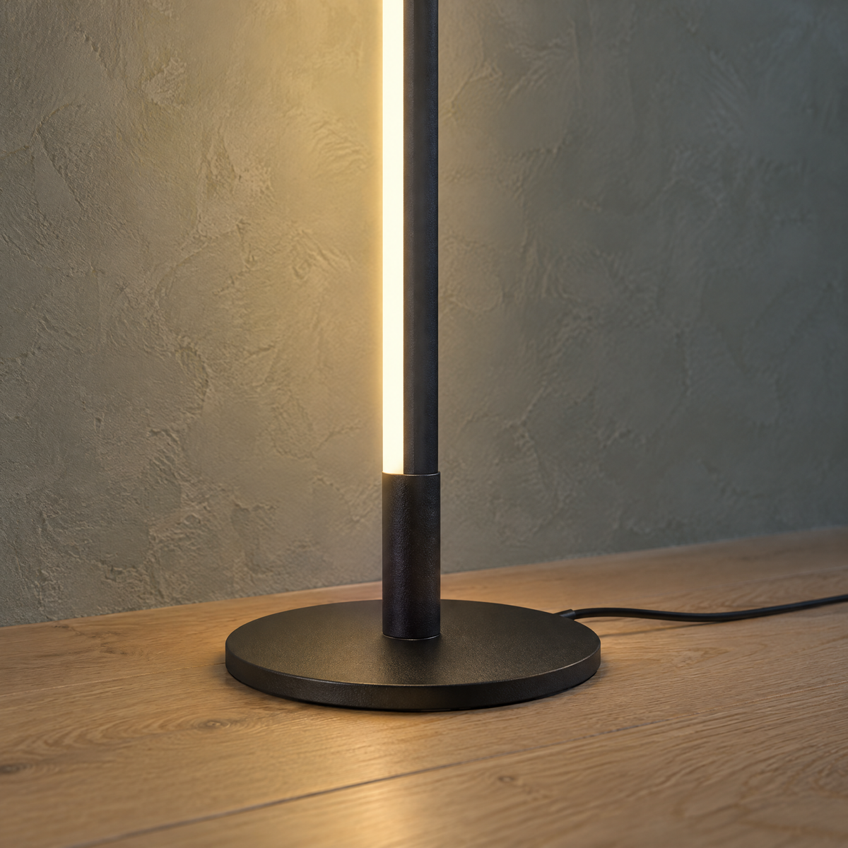 Detail der LED-Stehlampe: runder schwarzer Fuß, leuchtende Lichtleiste und Netzkabel