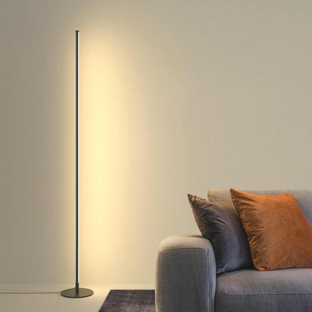Schwarze LED-Stehlampe neben einem grauen Sofa mit warmem Licht an der Wand